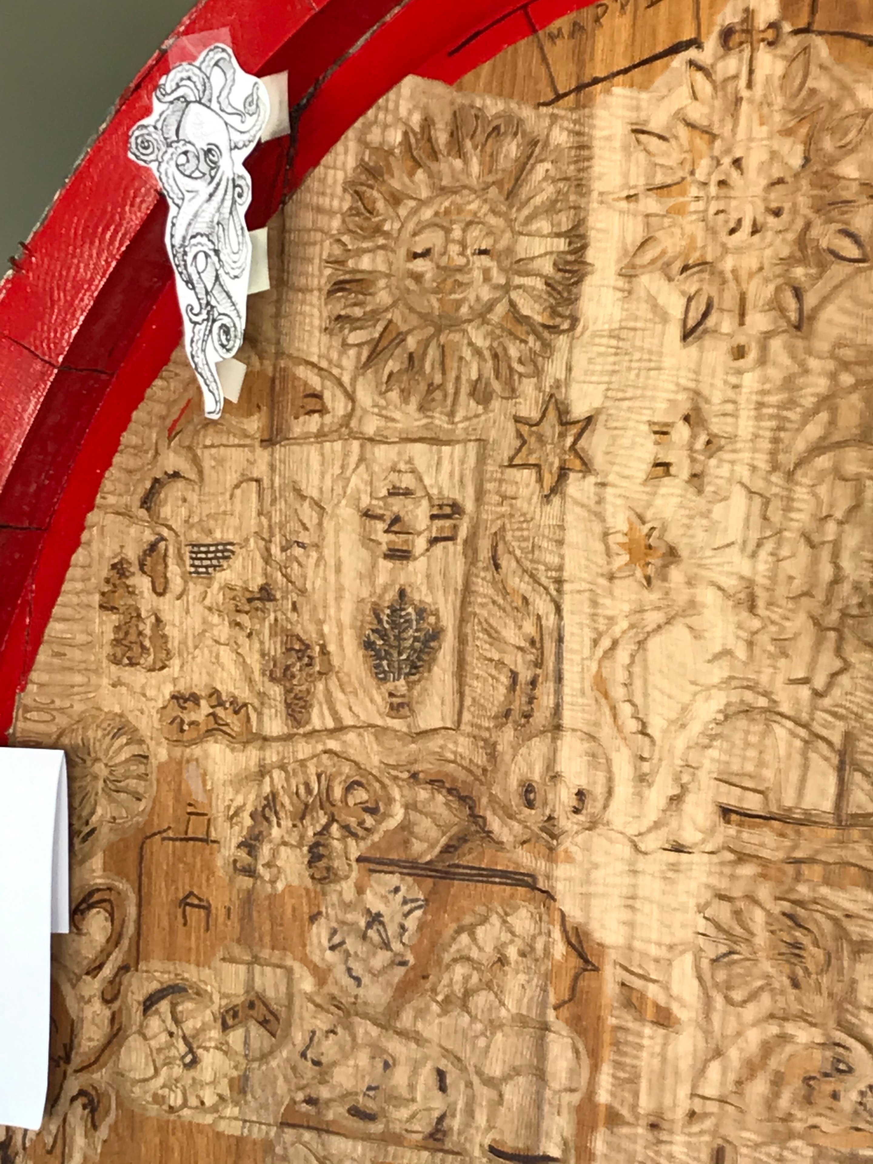 Close-up detail of hand-carved wine cask end with sun, village scenes and octopus sketch
