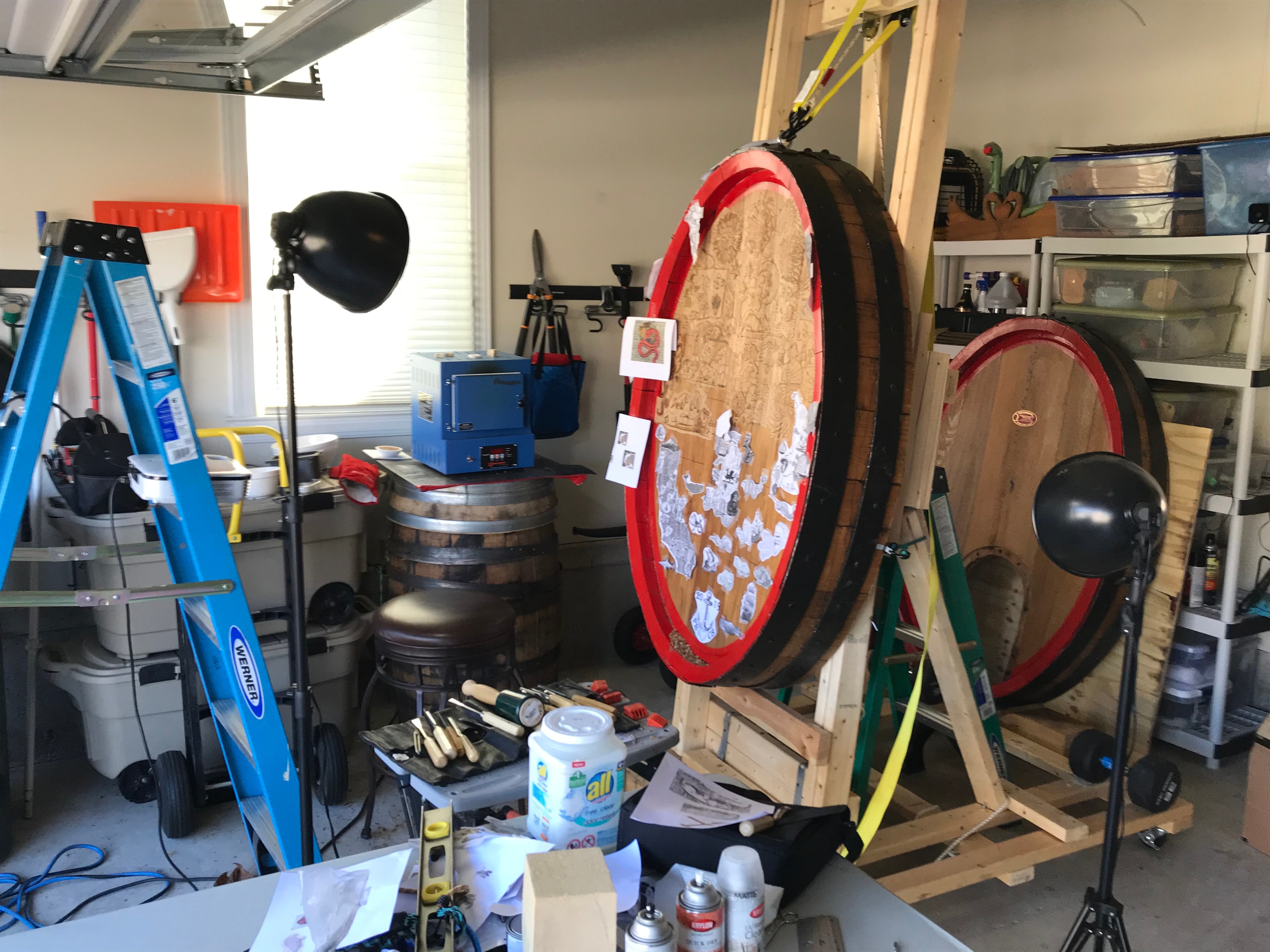 Workshop studio with two large wine cask ends on easels surrounded by carving tools and equipment